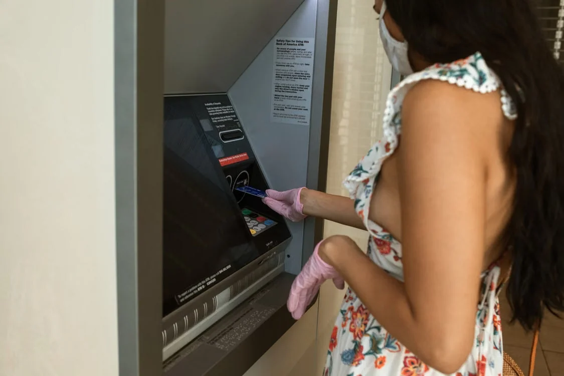 Maszkot viselő nő egy bankautomatánál kártyát használ.